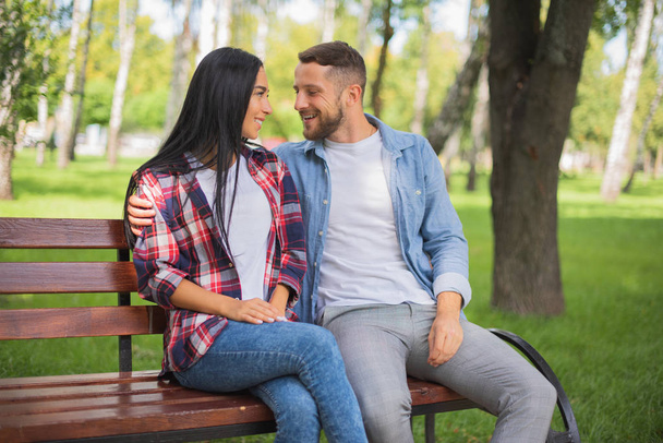loving couple in a park on a bench talking on the phone, handsome guy and girl - Foto, imagen