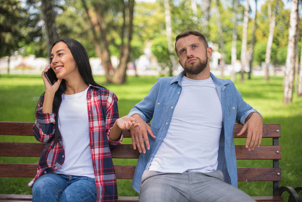 Liebendes Paar in einem Park auf einer Bank, telefonierend, gutaussehender Typ und Mädchen - Foto, Bild
