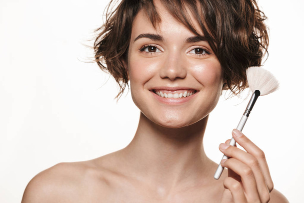 Young pretty woman with healthy glowy skin posing isolated over white wall background holding makeup brush. - 写真・画像