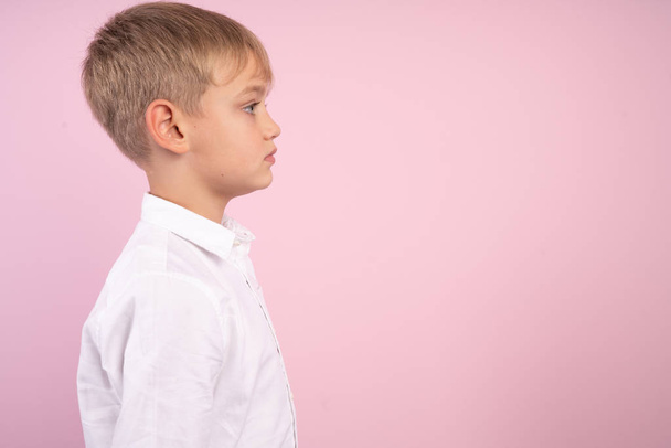 Profil małego cute Boy. portret Studio nad różowym tłem. ubrany w białą koszulę. Wolne miejsce na reklamę, logo lub tekst. - Zdjęcie, obraz