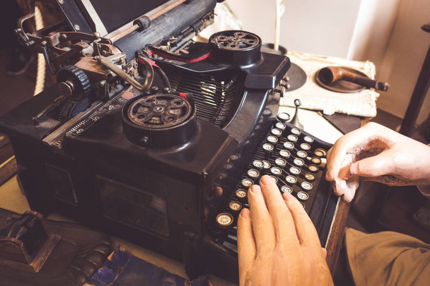 Vintage γραφομηχανή αντίκα με σωλήνα στο παλιό τραπέζι και το χέρι του γέρου δακτυλογράφηση επιστολή σε vintage στυλ γραφείου. - Φωτογραφία, εικόνα