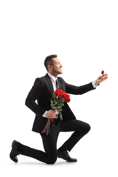 Young elegant man in a suit kneeling and holding roses and an en - Photo, image