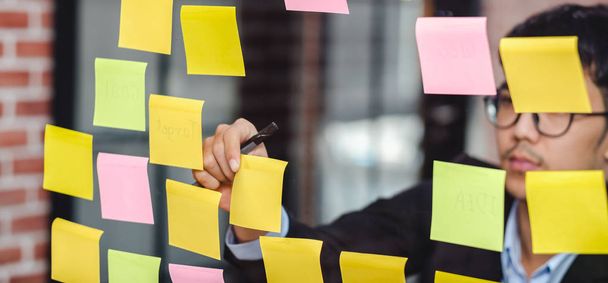 asian businessman looking and writing on sticky note for brainst - Foto, afbeelding