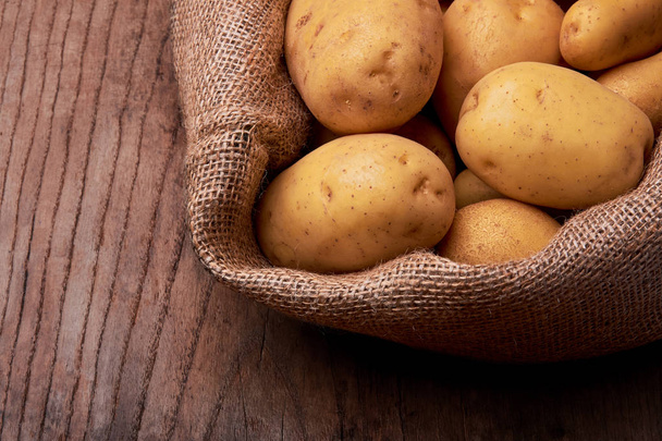 Uitzicht op stapel nieuwe aardappelen met jute zak op houten bureau. - Foto, afbeelding