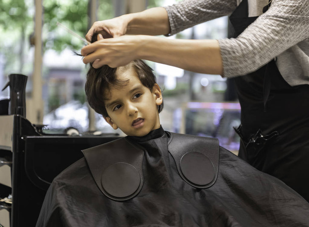 Friseure Hände machen Frisur für Kind kleiner Junge im Friseursalon Haarschnitt professionell - kleiner Junge im Friseursalon Haarschnitt professionell Kleinkind bekommt seinen ersten Haarschnitt neugierig - Foto, Bild