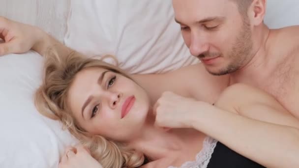 A young married couple, a man and a woman are lying on a bed with white linens. Morning and awakening. - Кадри, відео