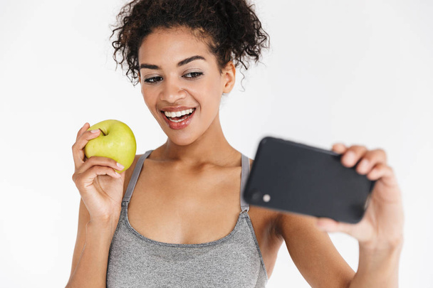 Beautful giovane incredibile sport fitness donna africana in posa prendere selfie con mela dal telefono cellulare
. - Foto, immagini