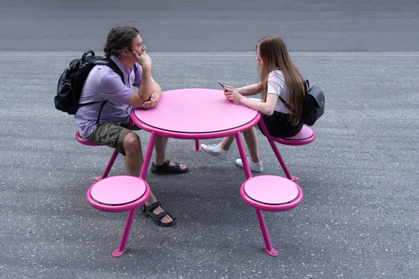 A young man and girl are sitting at a pink table in the street.  - Photo, Image