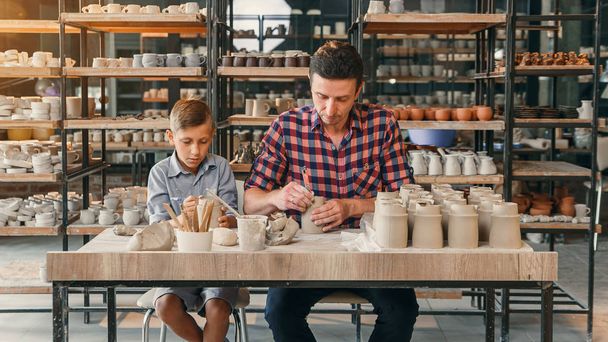 Little cute boy with his father making ceramic pots in the pottery. - 写真・画像