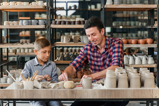 Seitenansicht eines Mannes mittleren Alters, der mit seinem kleinen Bruder in der großen Töpferei mit Keramiktöpfen arbeitet. - Foto, Bild