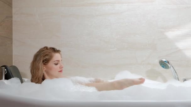 Beautiful young woman blonde lies in the bath tub with foam. Resting and relaxing. - 映像、動画
