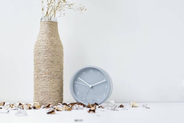 Classic alarm clock, flower branch and petals on a white table. Cozy winter or autumn background - Photo, Image