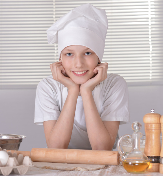 Young boy in a chef's hat knead dough for cookies - Фото, изображение