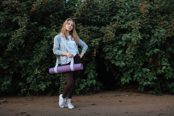 Фітнес жінка, що носить йога килимок з ремінцем на вегетативному фоні
 - Фото, зображення