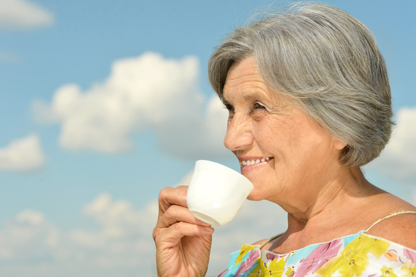 Elderly woman with cup on sky background - Zdjęcie, obraz