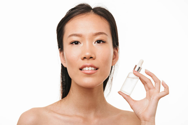 Young pretty woman with healthy skin posing isolated over white wall background holding serum oil. - Foto, afbeelding
