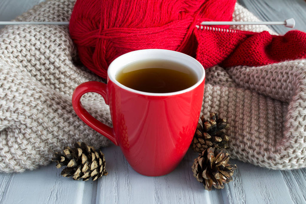 Taza de té, punto rojo y conos de pino en el fondo de la bufanda de punto
 - Foto, imagen