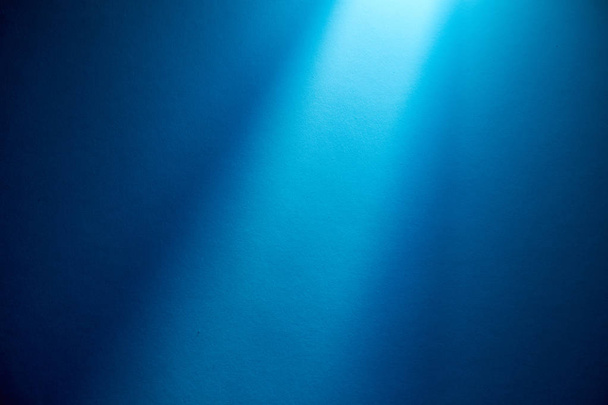 Light blue ray of light illuminates the blue fine-textured background from above - Photo, Image