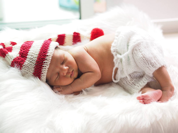 asiatisches Neugeborenes trägt eine gestrickte Weihnachtselfenmütze schlafend  - Foto, Bild