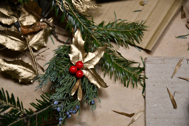 Zlatými malovanými listy s červenými bobulkami a jedle na hnědém řemeslním papíru. Zlaté pozadí textury. Lesklé zlaté pozadí. Zásobení zásob. Ručně vyrobené vánoční dekorace. Zimní výzdoba - Fotografie, Obrázek