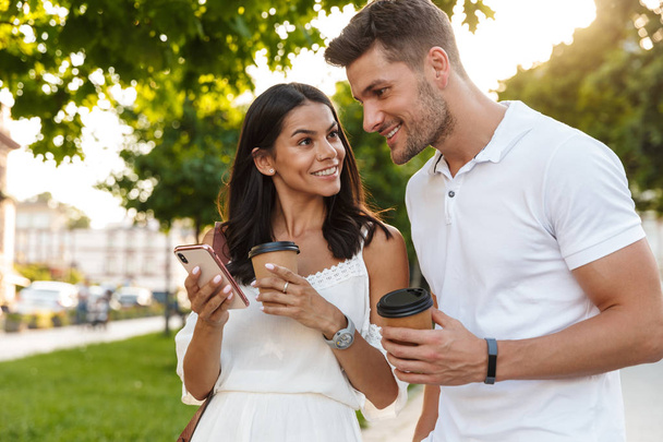 Portrait of brunette young couple using smartphone while walking - Photo, Image