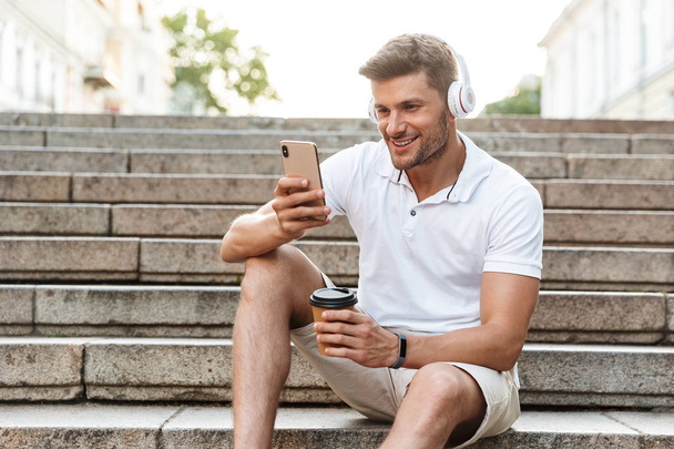 Πορτραίτο του όμορφου νεαρού άντρα με ακουστικά και smartphone w - Φωτογραφία, εικόνα