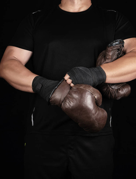 adult muscular man in black clothes puts on leather brown boxing - 写真・画像