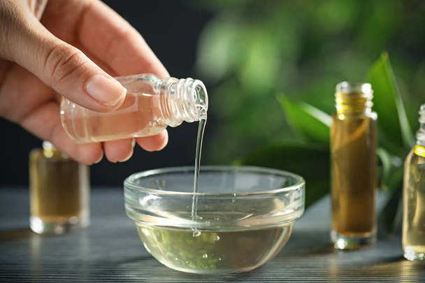 Woman pouring essential oil from glass bottle into bowl on table, closeup - Foto, Bild