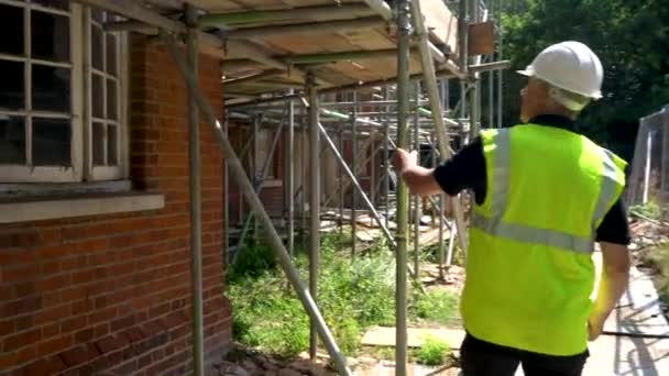 Male builder foreman construction worker on building site inspecting and checking scaffolding for health and safety - Video