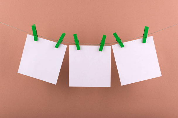 блокнот паперові листи для нот і нагадувань білого кольору, закріплені декоративними зеленими прищіпками, що висять на мотузці на бежевому фоні
 - Фото, зображення
