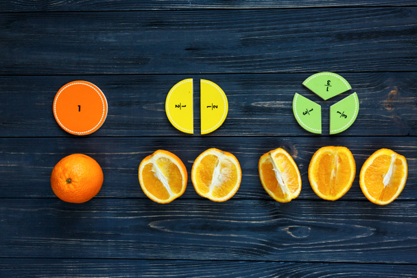 colorful math fractions and oranges as a sample on dark wooden background or table. Interesting creative funny math for kids. Education, back to school concept. Geometry and mathematics materials. - Photo, Image