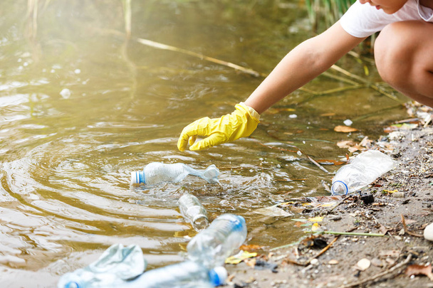 Junge in weißem T-Shirt und Handschuhen sammelt am Strand Müll und Plastikflaschen in blauen Verpackungen ein. junger Freiwilliger. Umweltschutz, Umweltschutzkonzept retten.  - Foto, Bild
