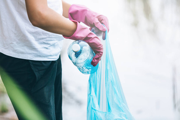 Niño en camiseta blanca en guantes recoge la basura y botellas de plástico en el paquete azul en la playa. Joven voluntario. Protección del medio ambiente, ahorrar concepto de medio ambiente
.  - Foto, Imagen