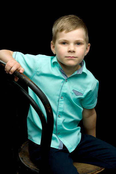 Smiling little boy sitting on stool, on a black background. - Fotografie, Obrázek