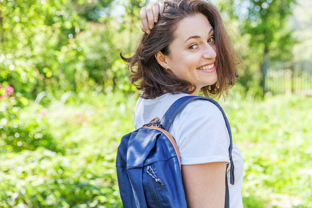 Heureuse étudiante positive avec sac à dos souriant sur fond de parc vert
 - Photo, image