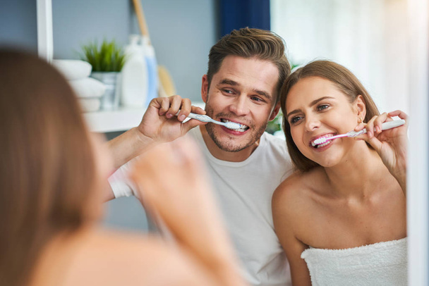 Portrait of happy young couple brushing teeth in the bathroom - 写真・画像