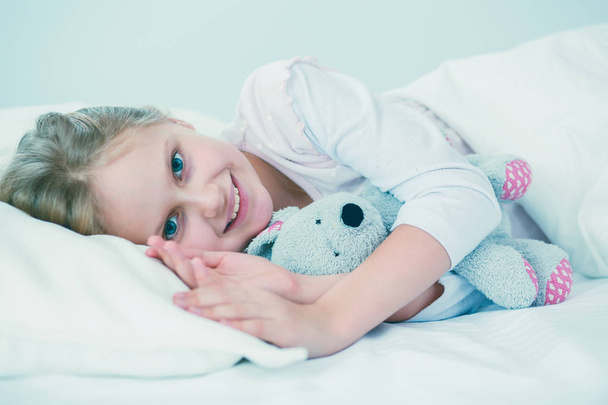 Child little girl sleeps in the bed with a toy teddy bear. - Foto, imagen