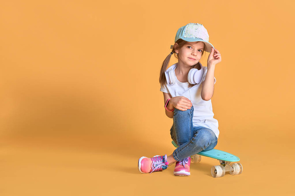 Stylish little girl child girl in casual with skateboard over yellow background - 写真・画像