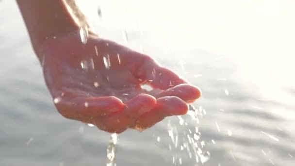 Ženská ruka, co si hraje s pitím vody na pozadí. Ženská ruka s kapkami vody zářící na slunci. Ženská ruka s kapkami vody na mořské pozadí. Neměstská scéna - Záběry, video