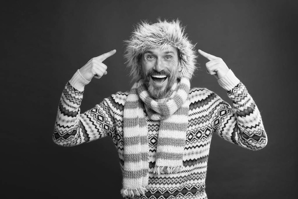 Wearing some key winter accessories. Bearded man in sweater and scarf pointing at hat. A winter ensemble protects him from cold. Mature fashion model in cold weather style. Winter wardrobe for man - Photo, Image