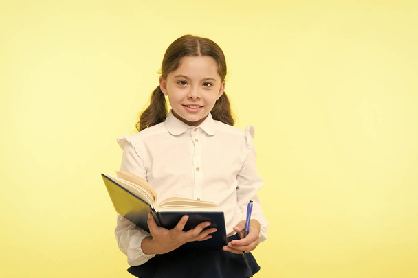 Child girl school uniform clothes hold book and pen. Girl cute write down idea notes. Notes to remember. Write essay or notes. Personal schedule. Making notes. Child school uniform kid doing homework - Fotografie, Obrázek