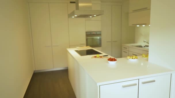 Современный стиль белых кухонных шкафов с плоскими дверями и ящиками, белая кухонная столешница из кварца и электрической плиты, декоративная еда и тарелки на ней. Концепция дизайна кухни
. - Кадры, видео