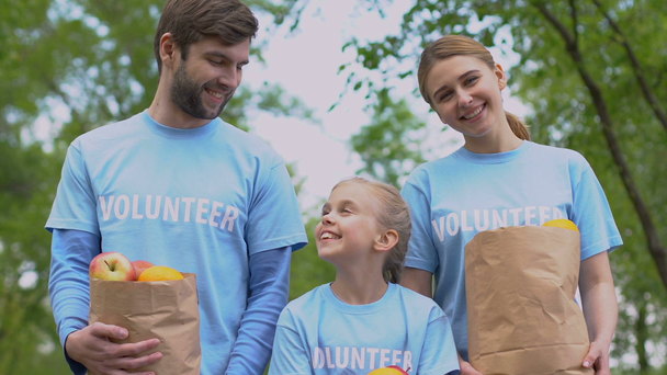 Χαρούμενα εθελοντές οικογένεια με μήλα χάρτινες σακούλες χαμογελαστά στην κάμερα, φιλανθρωπία - Πλάνα, βίντεο