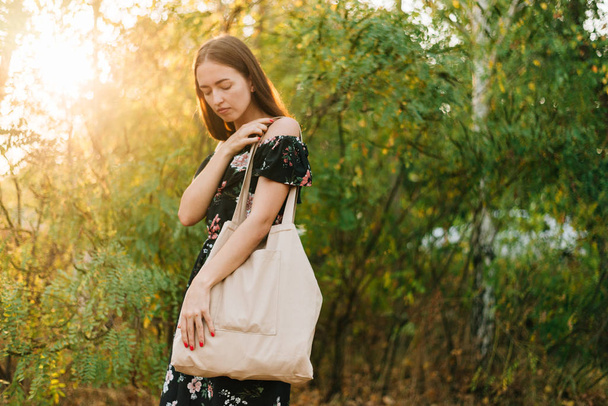 Caucasian girl holds linen shopper on sunset outdoors. Zero waste eco friendly conscious - Foto, afbeelding