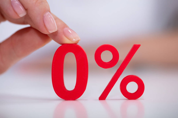Close-up Of Woman Holding Red Zero Percentage Icon Over White Desk - 写真・画像