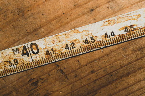 Old rusty ruler with black numbers on a working wooden table. vintage measuring tape. industrial background - Фото, зображення