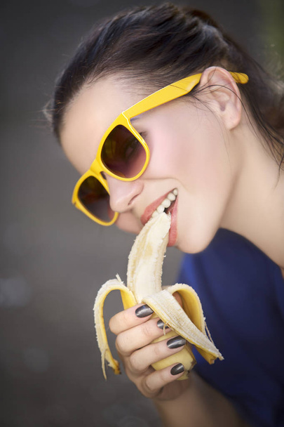 beautiful young woman in sunglasses eating a banana - Foto, afbeelding