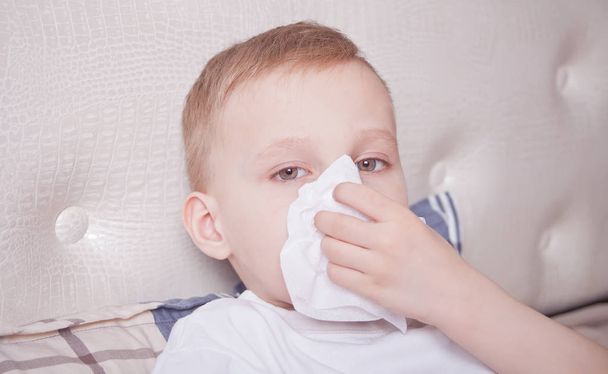 Sick boy lying in a bed and blowing her nose - Photo, Image