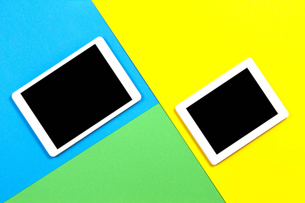 Two digital tablet computers on light blue, green and yellow background. Top view - Фото, изображение