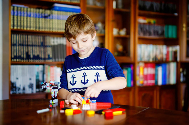Little blond dziecko bawią się wiele kolorowych bloków plastikowych. Cute chłopiec szkoły Kid zabawy z budynku i tworzenia robota. Kreatywna rozrywka Nowoczesna technika i roboty. - Zdjęcie, obraz
